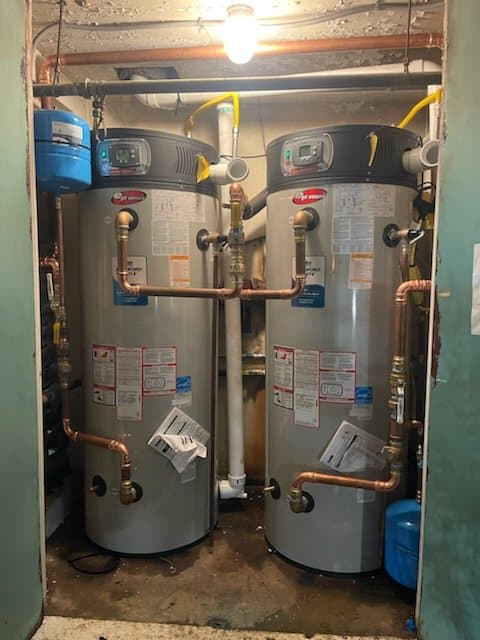 Two gas tank water heaters with copper connections and expansion tanks in a utility room, ready for routine maintenance — Alpha Omega Plumbing
