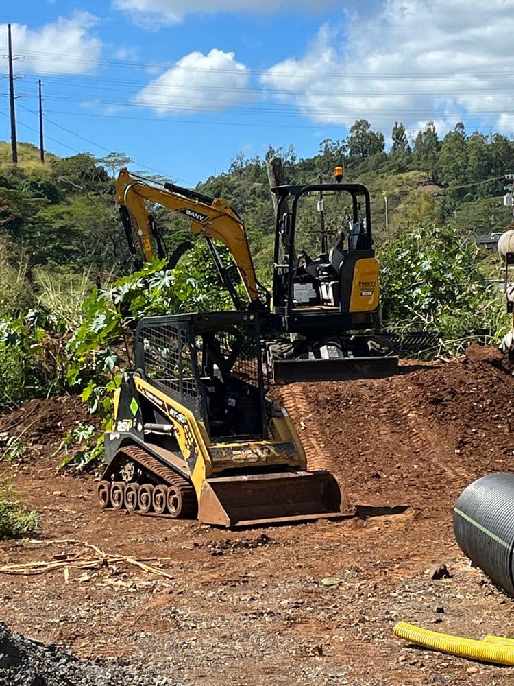 Excavator and track loader digging on a rural O'ahu property with drainage pipe ready for a septic system installation — Alpha Omega Plumbing